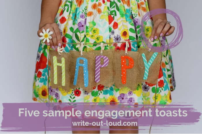 Girl, with a sparkling engagement ring, wearing a colorful flowery skirt holding a piece of burlap with the word 'Happy' on it.