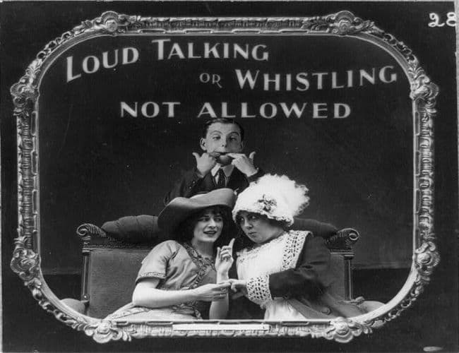Image: Two women talking. A boy behind them getting ready to whistle. One of a series of humorous  movie theater etiquette guides published 1912 by Scott and Van Altena.
